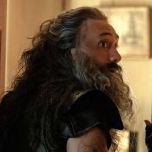 OFMD screencap: 1/2 view of Ed, long salt-and-pepper hair half tied up, looking over his shoulder to the right of the camera.
